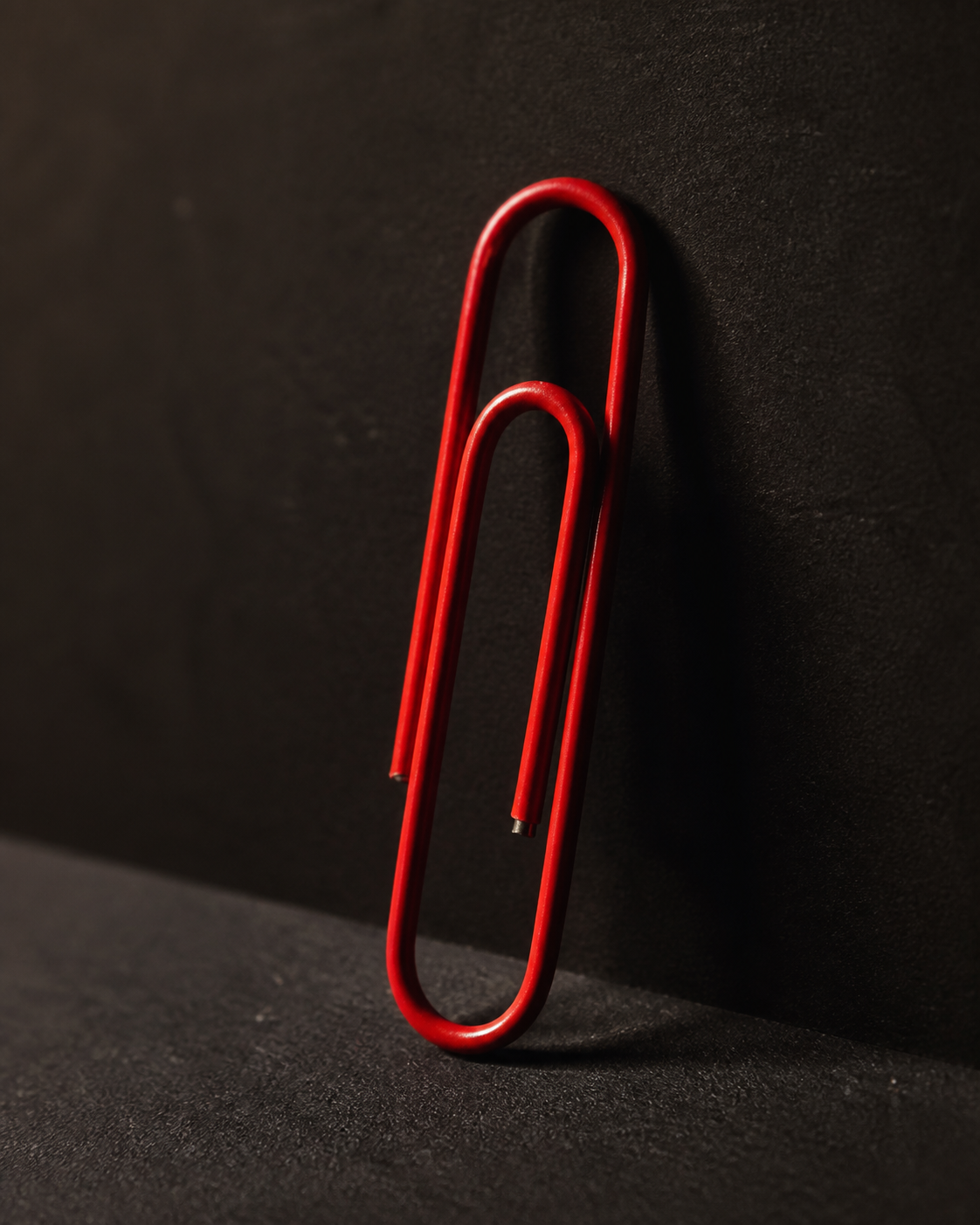 A jumbo red paperclip photographed under dramatic side lighting